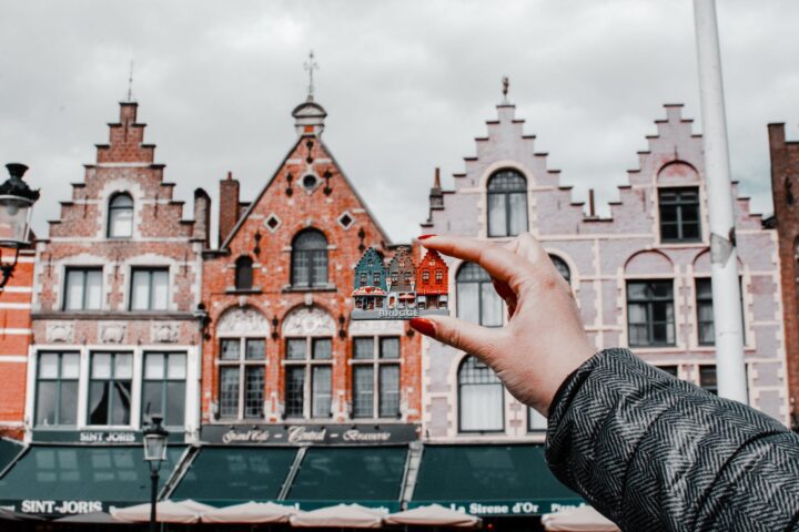 person holding miniature house toy comparing on real building