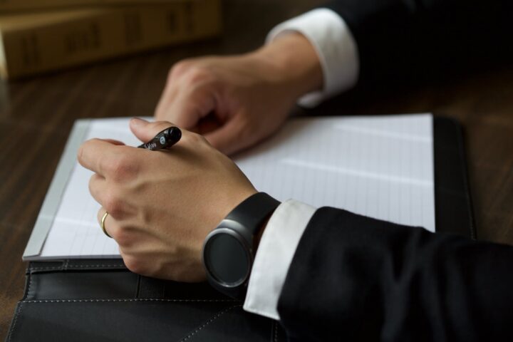 person on black suit jacket writing on white paper