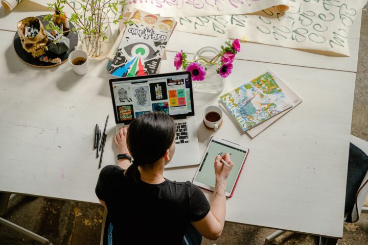 photo of woman writing on tablet computer while using laptop