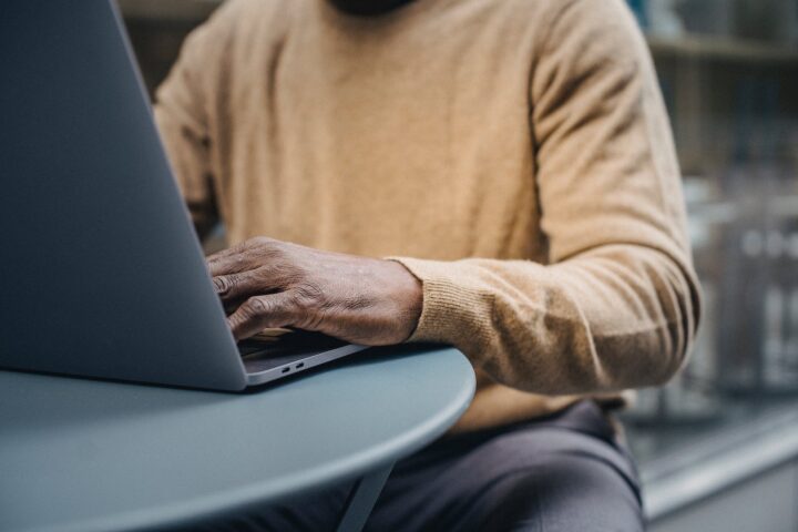 crop trendy african american man using laptop in street cafe