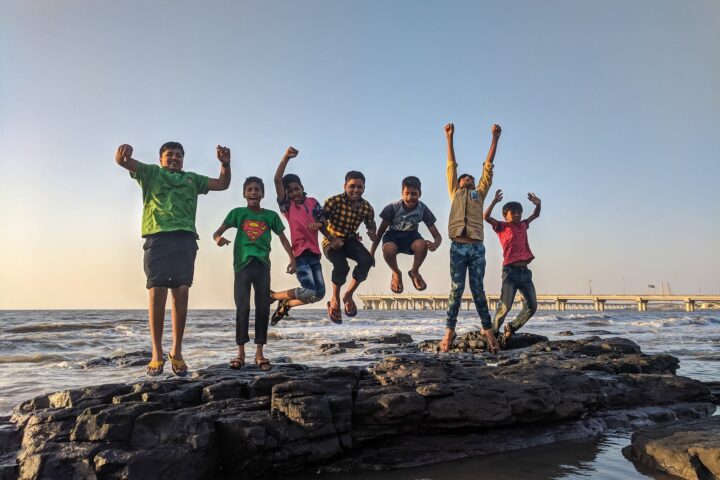 boy wearing green crew neck shirt jumping from black stone on seashore