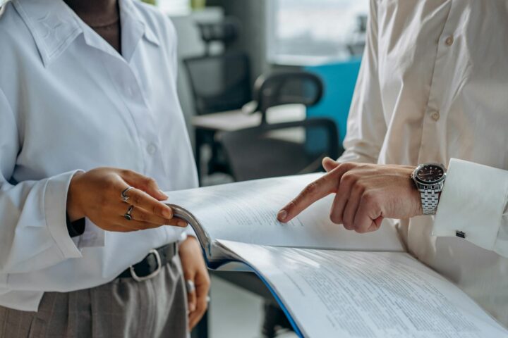 colleagues standing in white long sleeve shirts discussing and reading a financial report